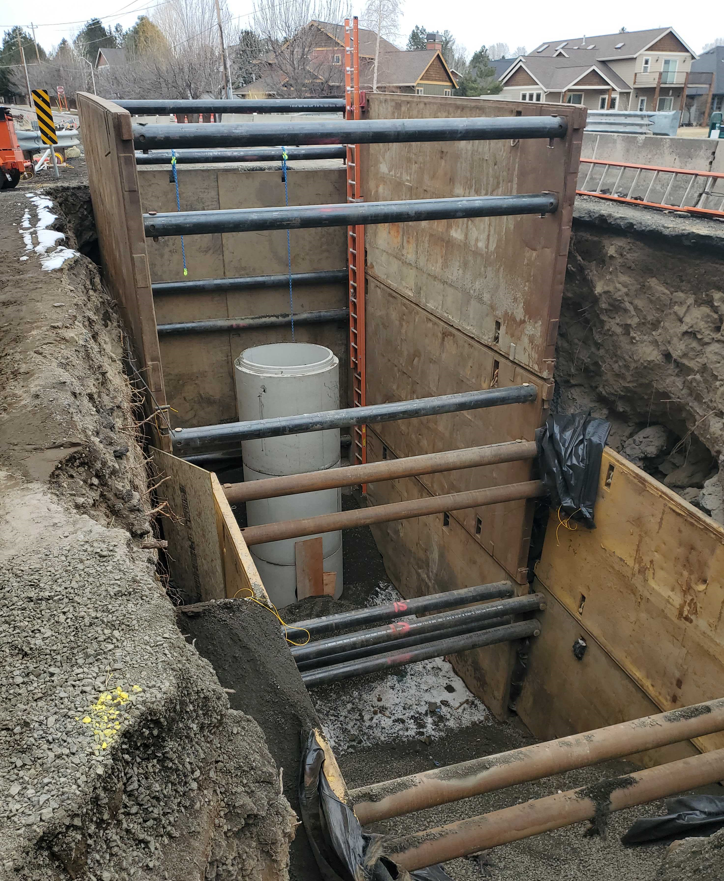 A photo of a partial maintenance hole installation in a large diameter trench that is reinforced with a trench box.