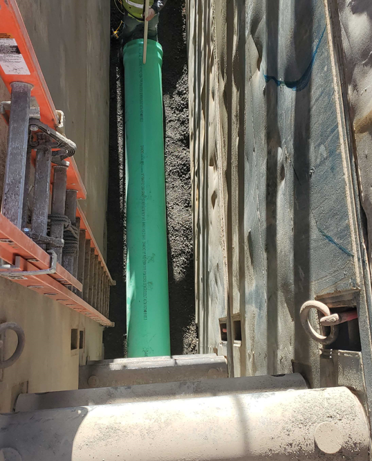 A photo looking approximately 17.5 feet down into a trench box showing the sewer pipe installation out of the King Solomon maintenance hole.