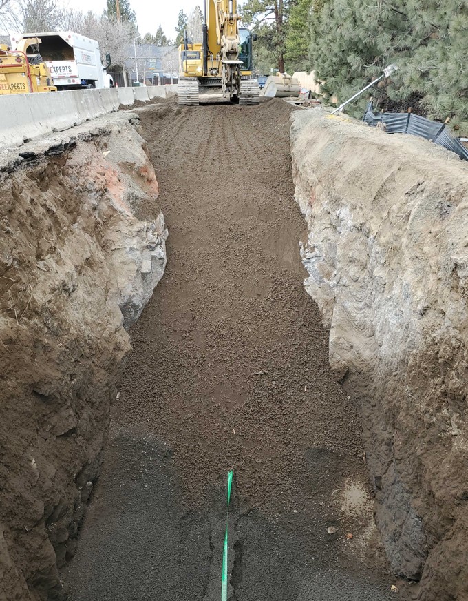 A photo of an excavator backfilling and compacting the sewer trench adjacent to the COID canal looking west towards King Solomon Ct.