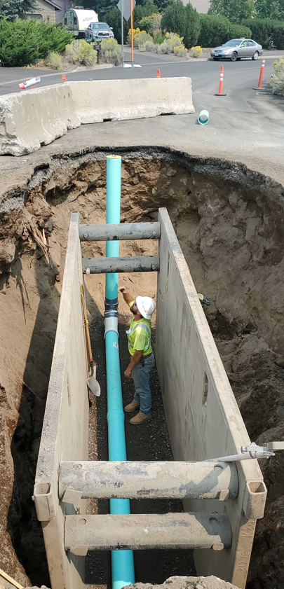 A photo of the sewer pipe termination at Ferguson Court (facing north). A crew member is in an trench working on the sewer termination inside of a trench box.