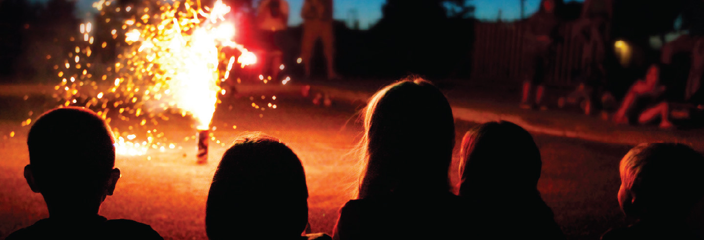 Children watching a firework throwing sparks on a street at dusk.