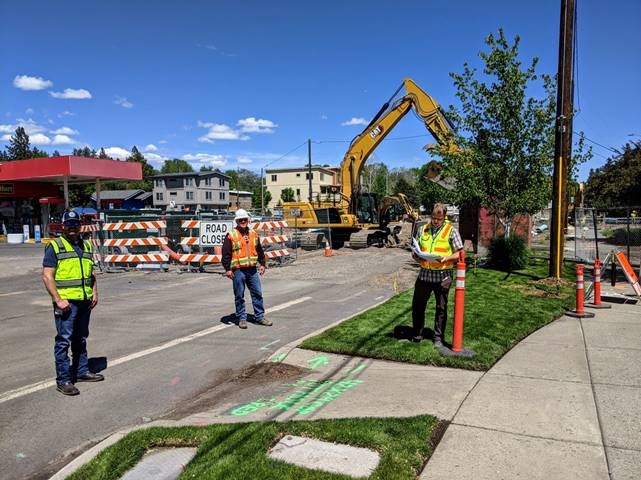 A photo of City Project Engineers and Inspectors standing on NW Newport Ave near NW Union St. There is a barricaded road closure, signs, cones, and large equipment in the background.