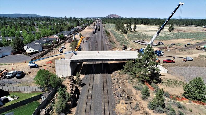 An aerial photo of the BNSF railroad tracks looking north at the new bridge. There are two cranes at the project site.