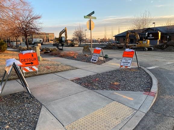 A photo of the Colorado Ave./Columbia St. intersection work zone with pedestrian traffic control signage along the sidewalk and construction equipment in the background.