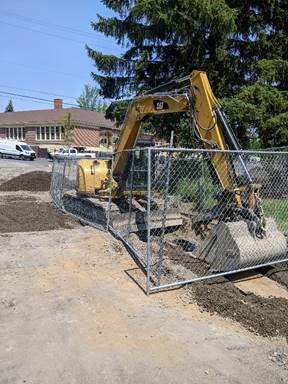 A photo of fencing placed around excavation equipment and an open trench.