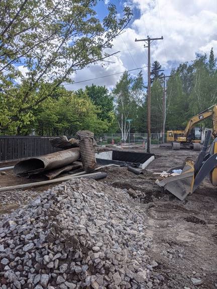 A photo of the existing stormwater pipe removed from Nashville Ave. There is a pile of excavated rock and excavation equipment working at the project site.