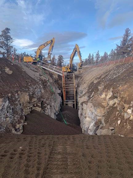 A photo of two excavators backfilling the pipe trench after pipe installation.