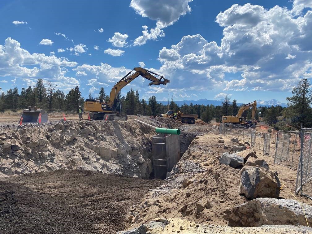 A photo of work crews and large equipment installing pipe in a large trench at Juniper Ridge.