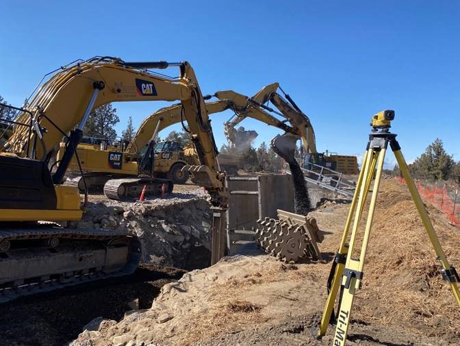 A photo of work crews using land surveying equipment and large excavation equipment for pipe installation at Juniper Ridge.