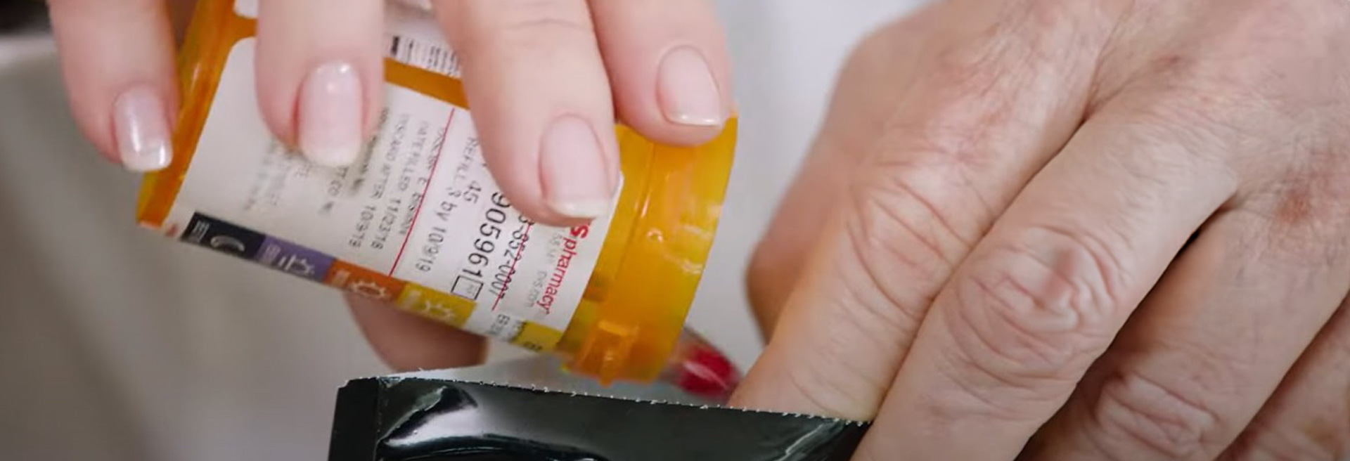 Closeup of hands dumping prescription drugs from a bottle into a black colored bag.