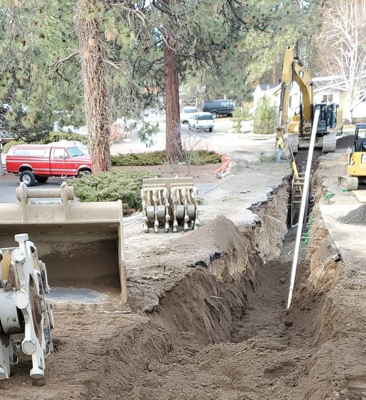 A photo of work crews installing new pipe in an excavated trench on Cinder Lane looking west.