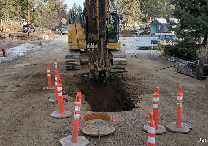 A photo of work crews using excavation equipment to excavate for new sewer in Ridge Drive heading north. There are cones and a barricade surrounding the excavation site.