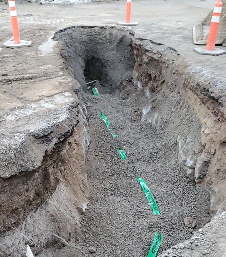 A photo of the tie-in to an existing sewer main in McMullin Drive. The excavated trench is surrounded by cones.