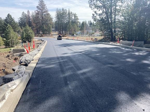A photo of work crews paving along Romaine Village Way, looking east.