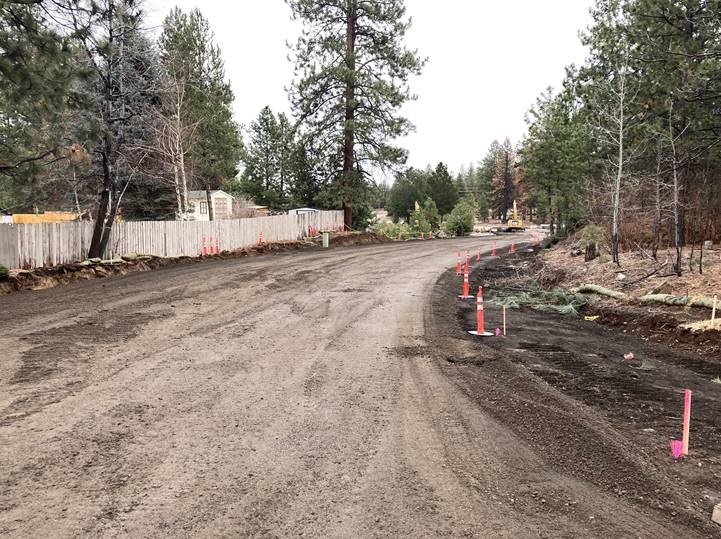 A photo of the realignment and grading work along Romaine Village Way. There are cones along the shoulder of the road and there's a large excavator further down the road in the background.