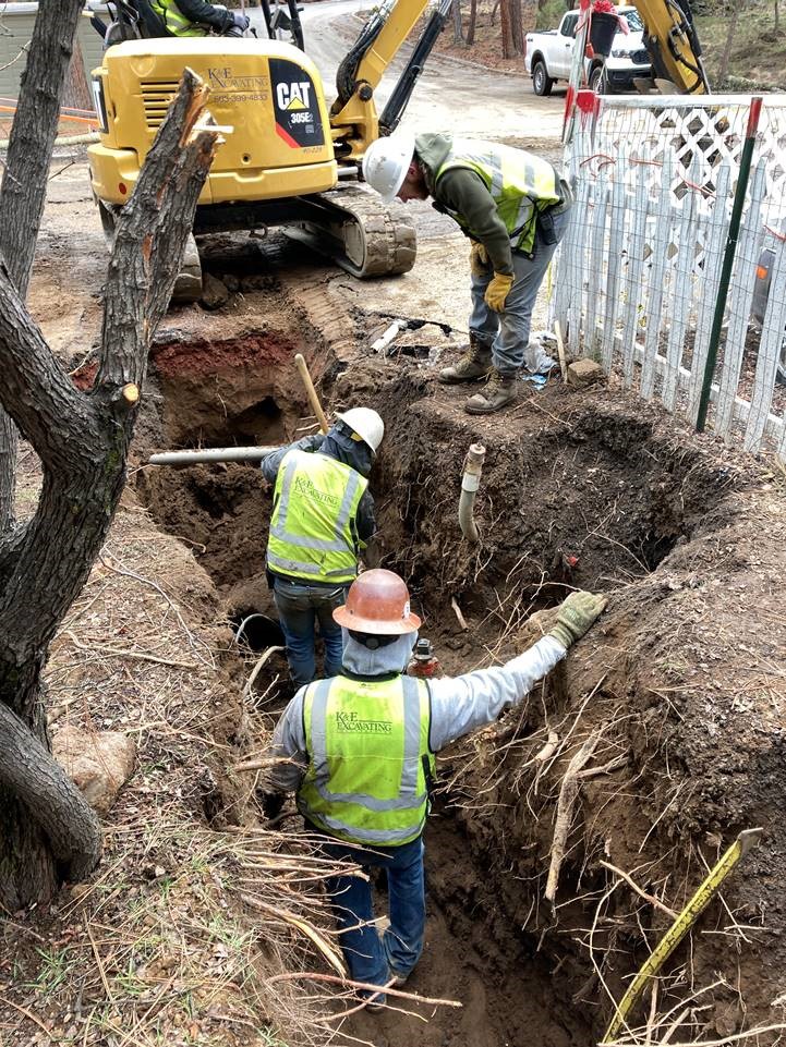 A photo of four work crew members and a small excavator performing excavation for new sewer services along McMullin Drive.
