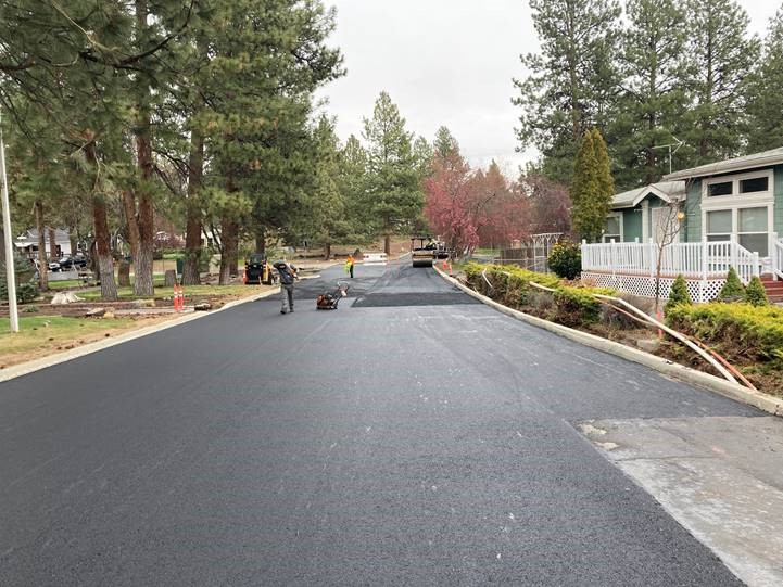 A photo of work crews laying the top, final layer of asphalt along Mahogany Street.