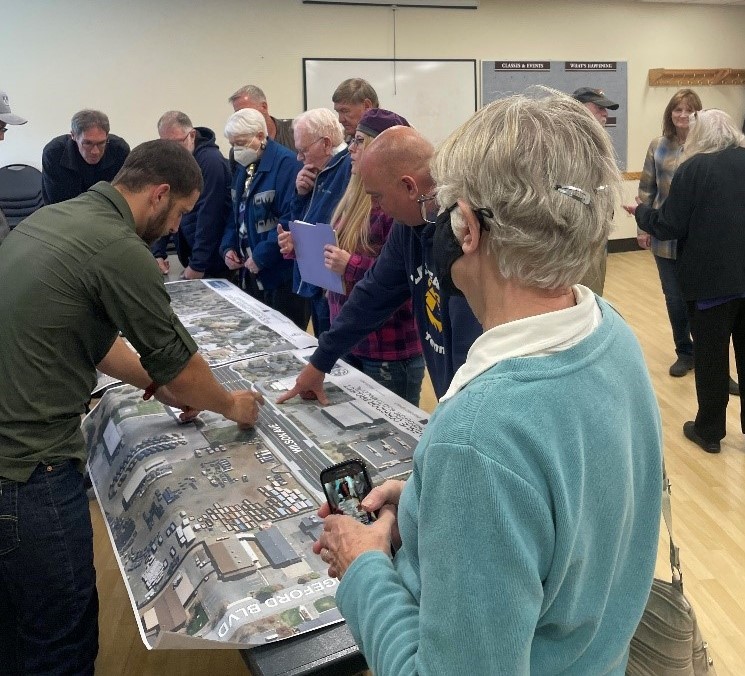 A photo of attendees conversing and viewing a large satellite view map exhibit at the April 27 open house event for the Wilson Avenue Corridor Project.
