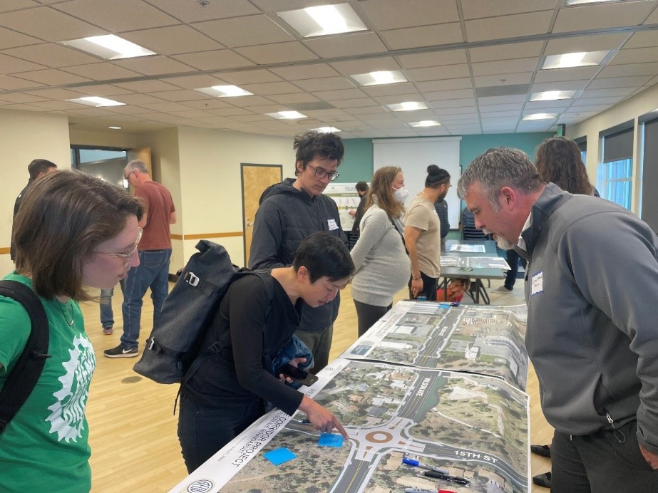 A photo of attendees conversing and viewing a large satellite view map exhibit at the April 27 open house event for the Wilson Avenue Corridor Project.