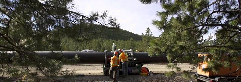 Imagine of large pipe being connected with another by two construction workers in the wilderness.