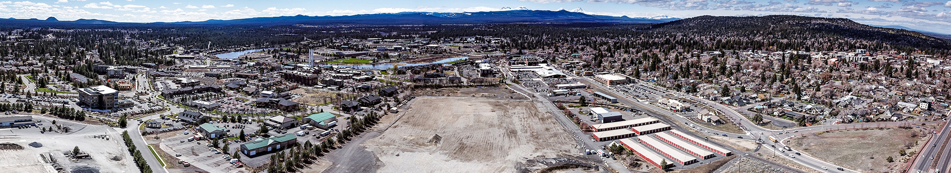 Overhead image of Bend's Core Area looking west towards the Cascade mountains. Empty lots, streets and commercial buildings are shown.