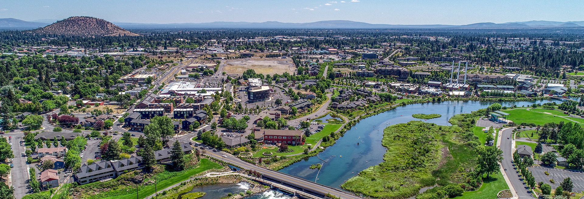 Bend looking northeast- Deschutes River in the foreground, Pilot Butte in the mid-ground. Parks, buildings, homes and streets.
