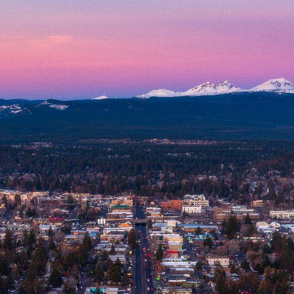 Bend at sunrise, sky is red and purple, snow capped mountains in the background.