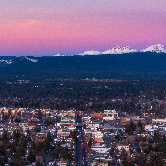 Bend at sunrise, sky is red and purple, snow capped mountains in the background.