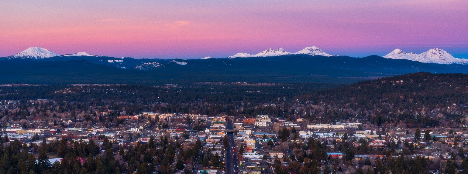 Bend at sunrise, red and purple sky, snow capped mountains in the background.