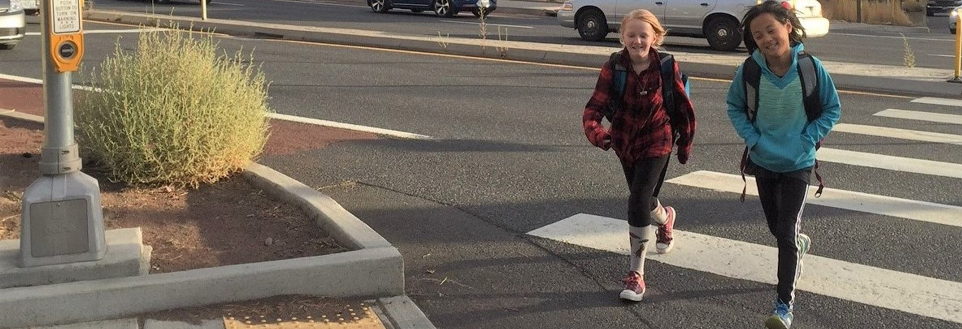 Two children crossing a busy road via a protected intersection.