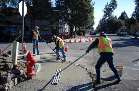 Street crew workers leveling new concrete at corner to prep for curb ramp installation.