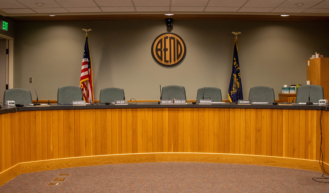Dias in City Council Chambers. The front is a light brown with chairs behind it.