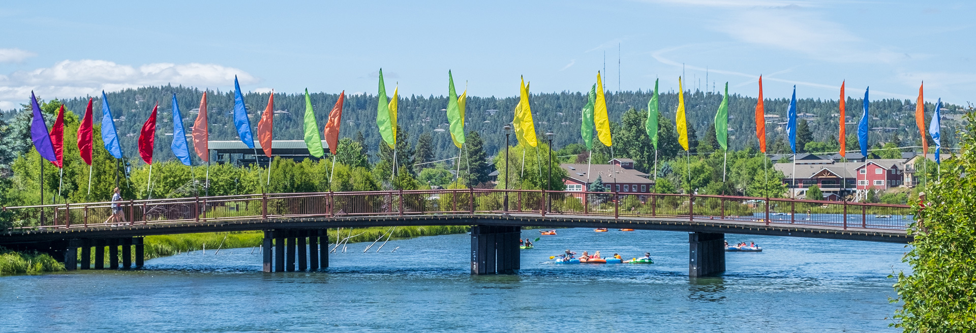 Footbridge over the Deschutes River with a railing with muti-colored flags flying from the top of the railing.