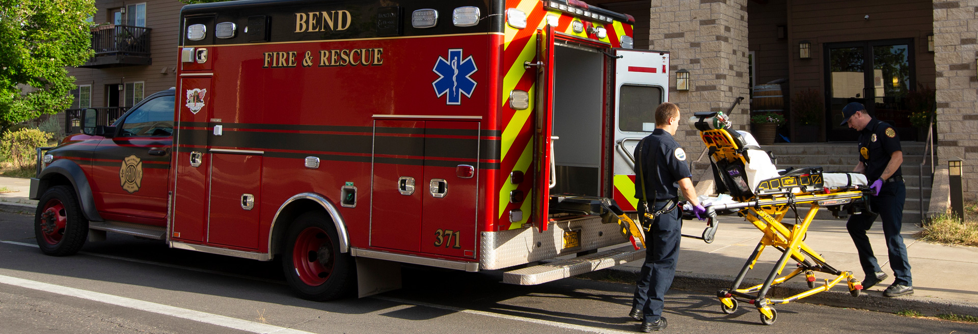 Two first responders moving a gurney out of the back of an ambulance.