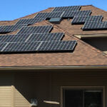 Solar Panels on top of a residence. Blue sky in the background. Home is brown in color.
