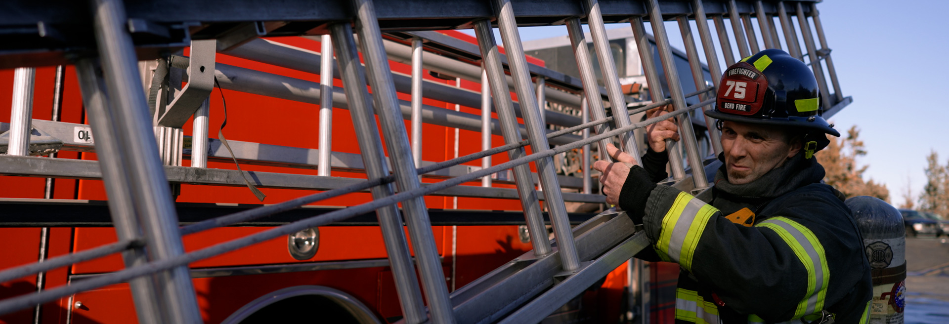 Firefighter removing a ladder from a fire engine and carrying it on his shoulder.