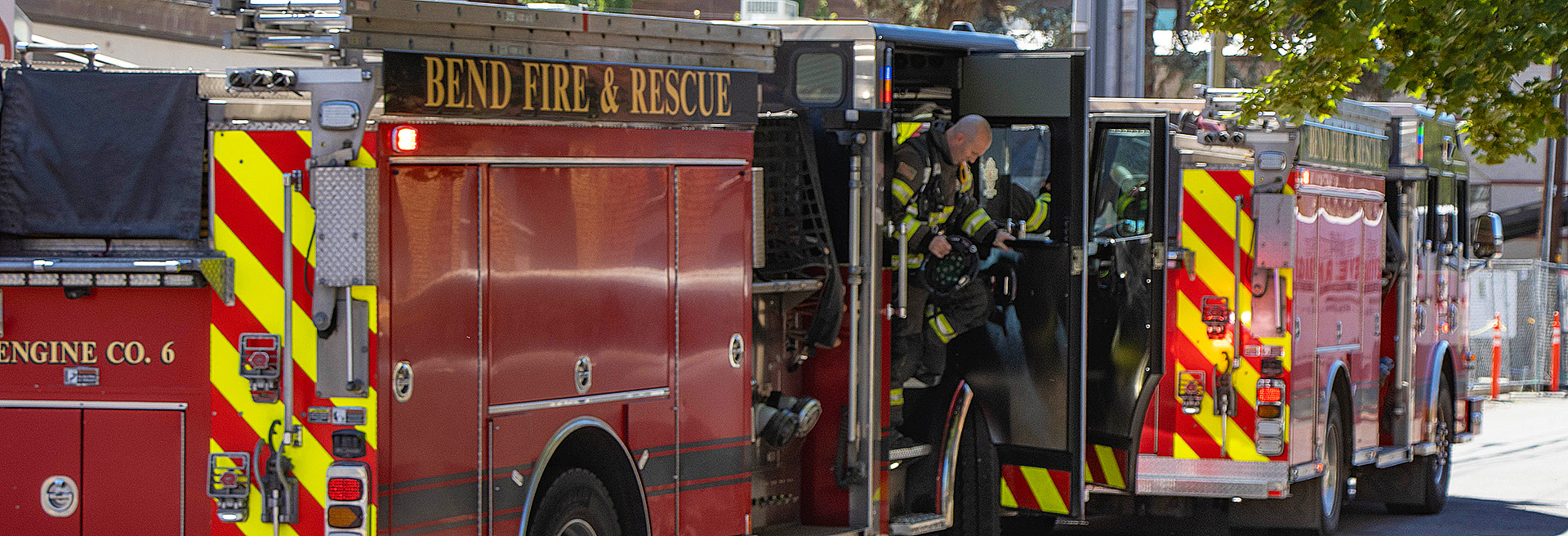 Two red fire engines parked on a street with a firefighter exiting the doors of one.