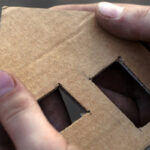Hands holding a cardboard cutout of a house.