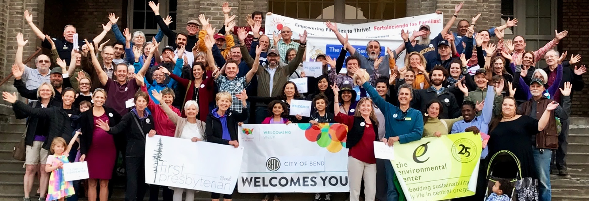 Large group of diverse people holding up signs and raising their hands in celebration.