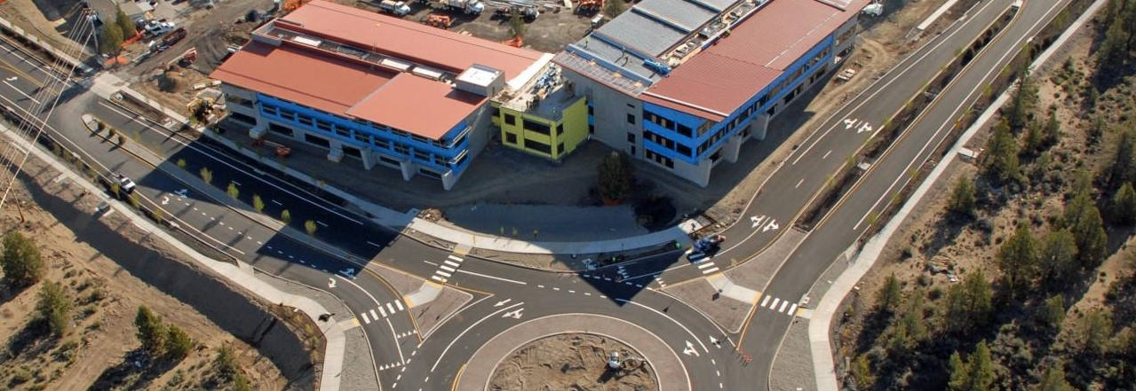 Overhead shot of a large commerical building under construction, bordering a roundabout for transportation.