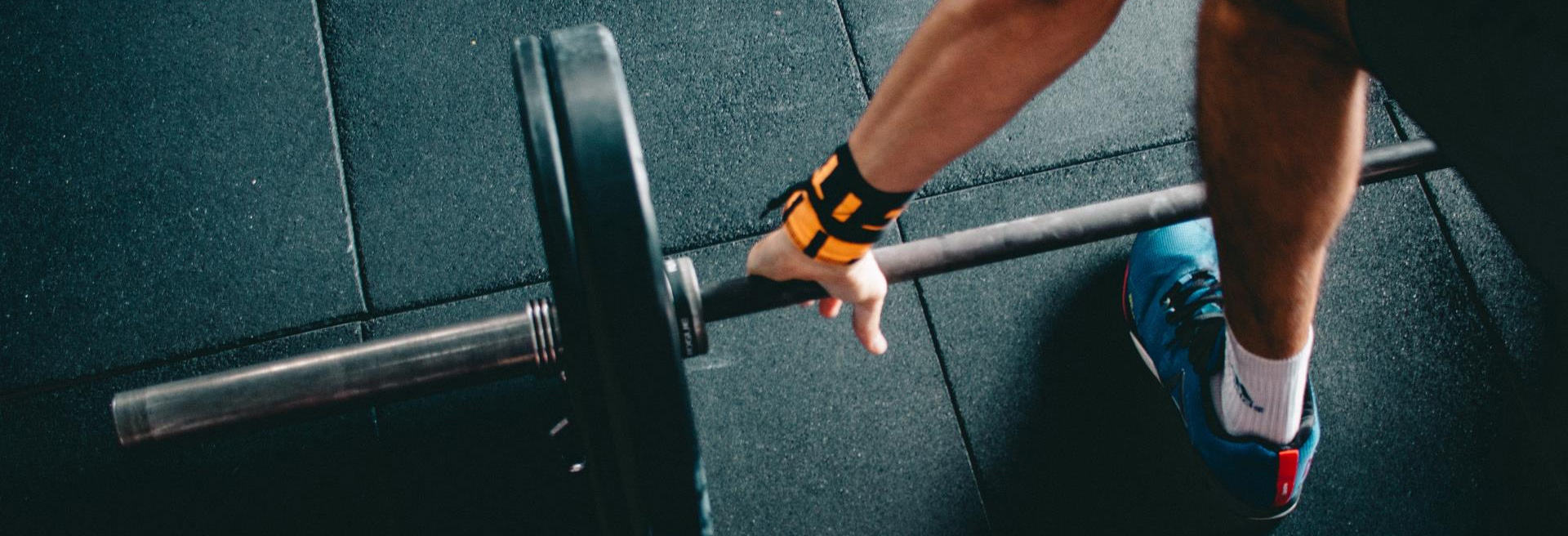 Looking down at a floor with a barbell on it and a person reaching to grab it.