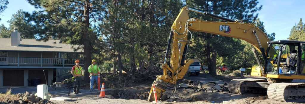 Workers surrounding a backhoe digging into a city street.
