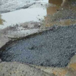 Pothole on a street with water puddles around it.