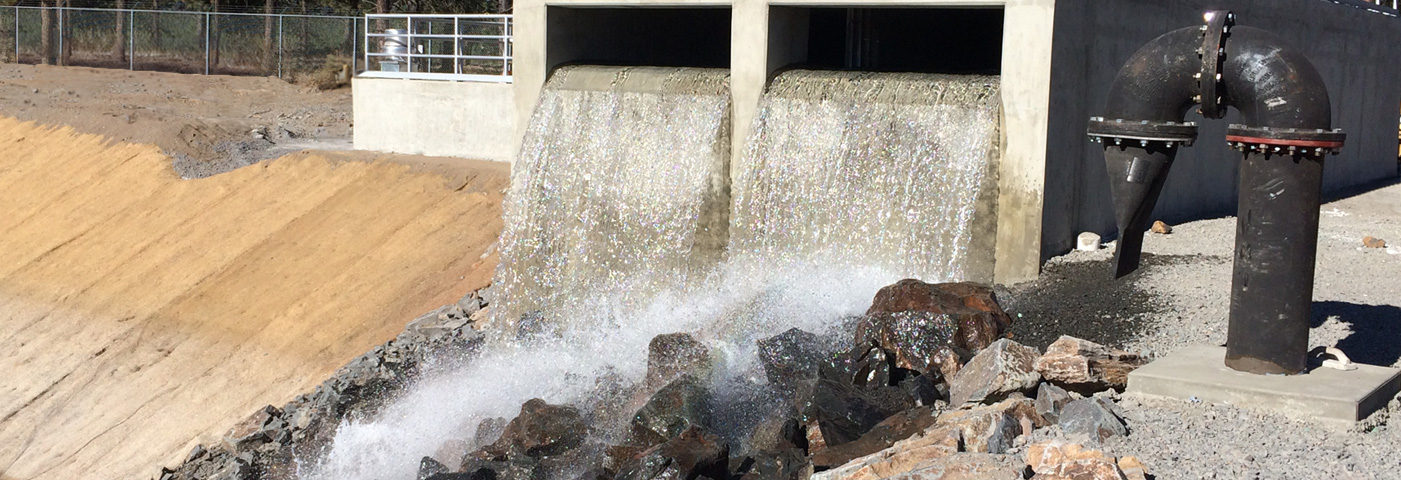 Water runoff through a cement barrier. Graded brown dirt surrounds.