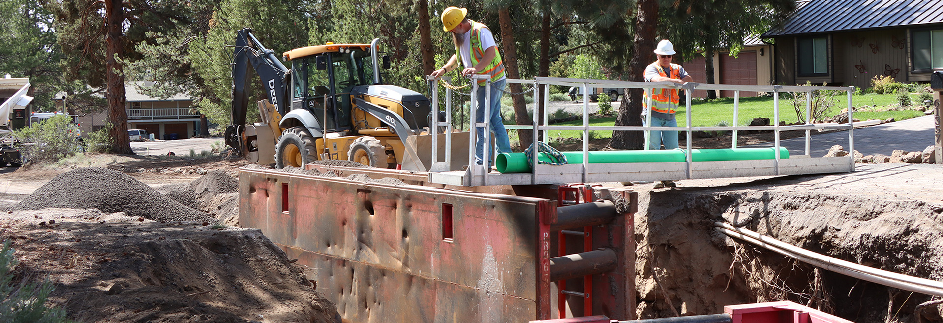 Construction workers working in a ditch using a backhoe in a street.