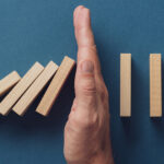 Dominoes falling with a hand stopping them on a blue background.