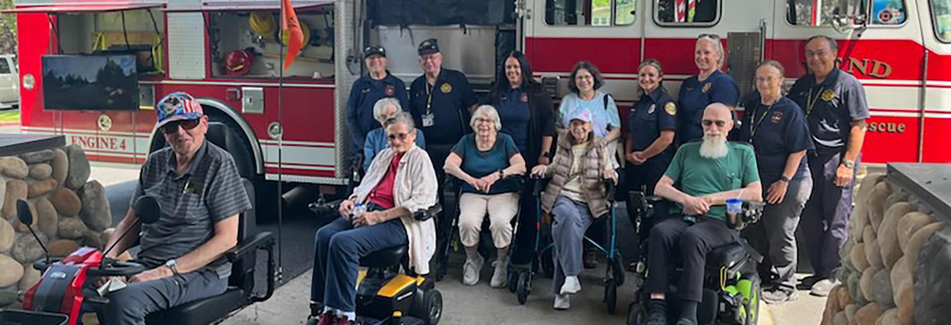 Group of senior citizens with Fire & Rescue personnel, sitting in front of a red fire engine.