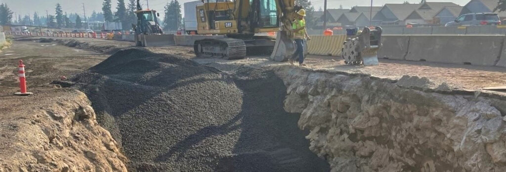 Ground excavated opening the earth for a new sewer line. A construction worker and backhoe are above the hole working.