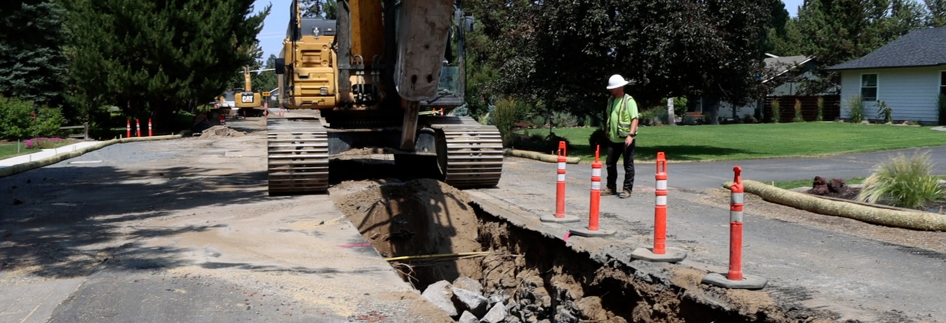 Construction workers working in a ditch using a backhoe in a street.