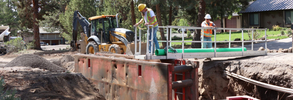 Construction workers working in a ditch using a backhoe in a street.